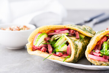 Egg rolls filled with pastrami, vegetables and green onions on a plate on the table. Hearty and high-calorie snack. Close-up