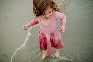 Young girl in wet pink dress wading in ocean