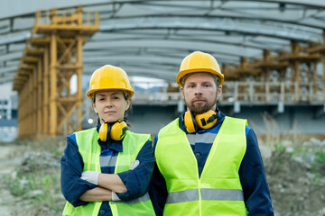 Two serious construction workers in uniform and helmets standing next to one another