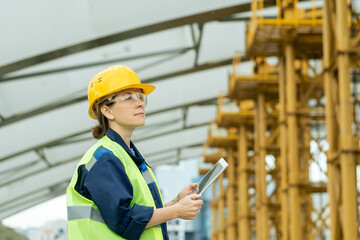 Happy female engineer with tablet looking at huge construction frame