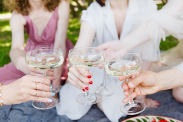 
A picnic, a meeting of girls or a bachelor party in a beautiful blooming garden in spring. Girls in light dresses drink champagne and eat pizza in the park
