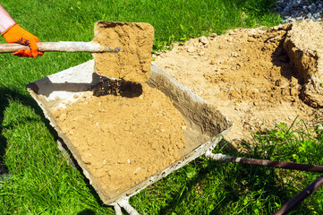 A master builder shovels sand into a cart to prepare concrete. Close-up of a master hand during...