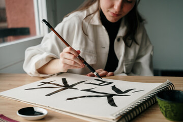 Young woman writing japanese kanji characters with a brush and ink