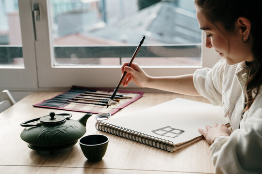 Young woman writing japanese kanji characters with a brush and ink