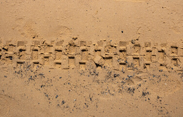 The texture of wet brown sand with traces of bicycle tires