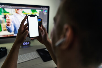 Close up image of smart phone mockup, businessman holding phone with white screen template in front of desktop computer. Empty space for ads massage, smart phone mockup