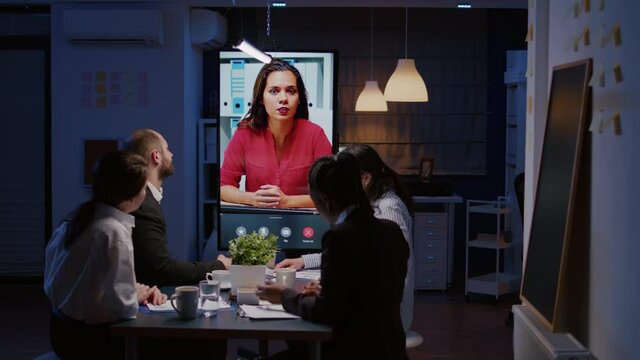 Workaholics multi-ethnic businesspeople discussing financial strategy during online videocall meeting conference overworking in office room late at night. Remote businesswoman solving company problem