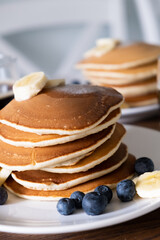 Stack of Tasty American style pancakes with a piece of butter, banana and blueberry on a white plate. Breakfast for two or weekend brunch