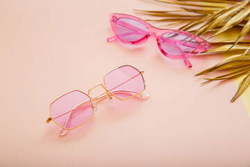 Pink gold colored Stylish sunglasses on color summer background with gold palm leaves. Fashionable trendy optics collection.