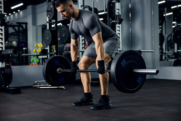 A portrait of a male weightlifter in grey sportswear. He does barbell fitness workout in the modern...