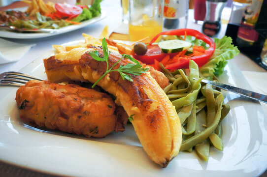 Fish espada with fried banana, french potatoes, kidney beans and fresh vegetables.