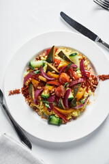 Vegetable stew with coarsely chopped zucchini, carrots, eggplant and bell pepper, top view, white plate on a white plate.