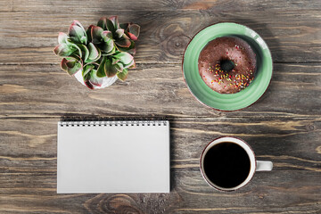 Coffee break in a cafe for inspiration. A break during work. Blank notepad, coffee cup and donut on a wooden table. Place for text, advertising background.