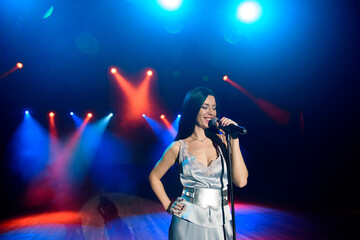 A female singer holding microphone against the colorful lights of the scene. Bright background with neon lights.