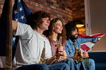 International group of student friends hanging out at home huddled on couch together excitedly watching event on TV drinking beer, anticipating winning goal. american football, basketball, tennis