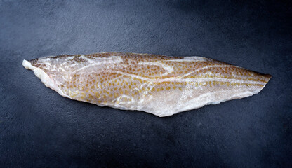 Raw Norwegian skrei cod fish filet with skin offered as top view on black board with copy space