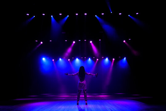 Unrecognizable singer standing on stage at microphone, back view, neon lights