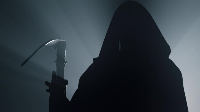 Silhouette death with scythe indoors. Man in costume grim reaper on halloween .