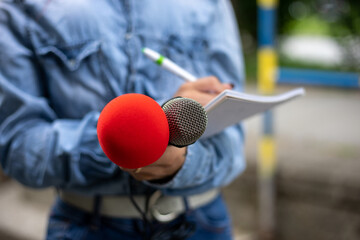 Journalist at news conference, writing notes, holding microphones