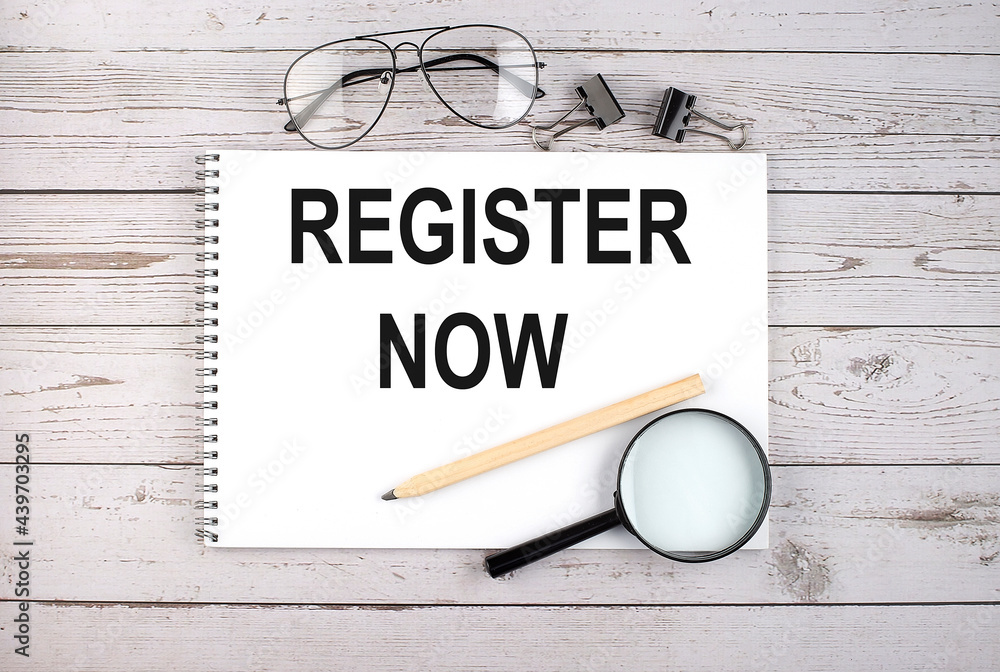 Poster notebook with text register now on the wooden table with pen, magnifier and glasses