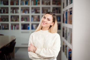 Girl student in the university library, in the background shelves with books.