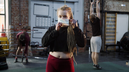 A strong athletic woman is putting on her face a mask and crossing her hands