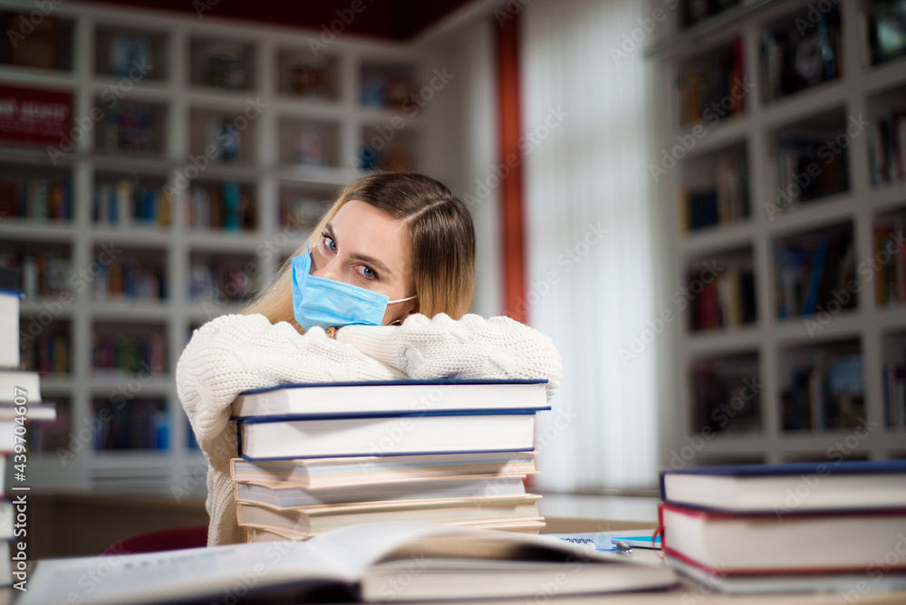 Wall mural A tired student in a protective mask for the face studying in the school library.