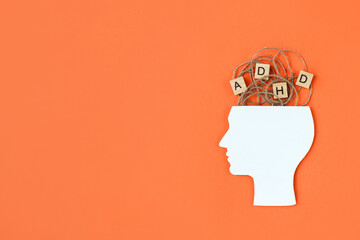 Silhouette of human head and wooden blocks with the letters ADHD on orange background. Minimal concept of attention deficit hyperactivity syndrome. Copy space - obrazy, fototapety, plakaty