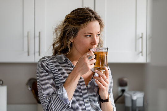 Beautiful Woman Sips Tea While Staring Out Kitchen Window