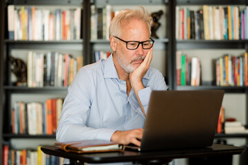 Tired Man Looks at His Laptop While Working From Home