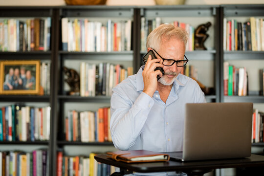 Older Man Uses Cell Phone and Laptop While Working From Home