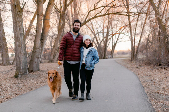 Smiling Couple Walks Dog in Park
