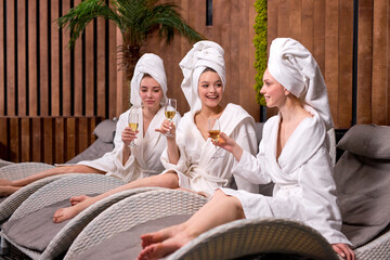 Gorgeous females in bathrobes and towels enjoying holidays in spa center, drinking champagne, alcohol beverage. Beauty procedures, spa, celebration, friendship, people, healthy lifestyle concept