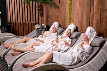 Relaxed ladies enjoy drinking champagne at spa. Three beautiful caucasian women wearing bathrobes...