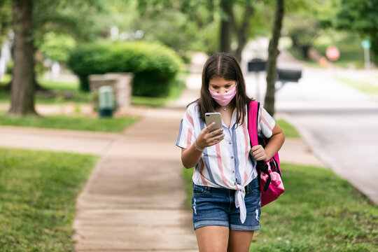 Student: Teen Girl With Face Mask Looks At Phone On Way To Schoo