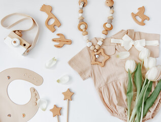 Newborn bodysuit with wooden toys and fresh tulips  on white background, top view, flat lay. Summer baby concept