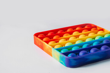 The square-shaped pop it anti-stress toy lies sideways. Rainbow touch fidget isolated on white background. New fashionable silicone toy.
