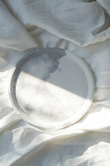 Empty round tray on white textured linen background, designer jewelry plate