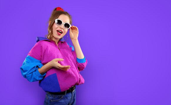 Cool teenager. Fashionable DJ girl in colorful trendy jacket and vintage retro sunglasses enjoys style of 80s � 90s vibes. Teenager Girl at disco party. Young fashion model on pink color background.