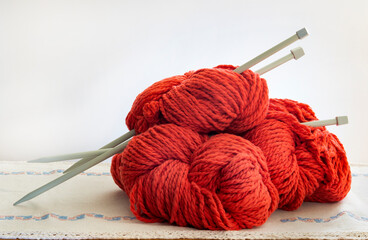 balls of thick red wool rolled and knitting needles