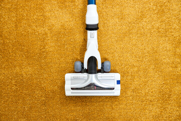 Close-up photo of vacuum cleaner applied on yellow carpet at home removing dust, cleaning at home,...