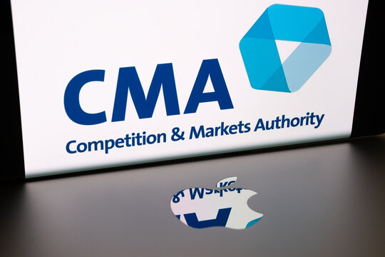 Apple logo on macbook surface and blurred UK CMA Competition and Markets Authority logo seen on the smartphone screen.  Concept. Stafford, United Kingdom, June 15, 2021.