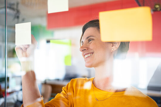 Businesswoman Putting Post-It Notes On Glass Board