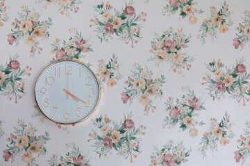 Horloge en or rose et blanc sur fond de tapisserie florale avec les aiguilles qui indiquent l'heure...