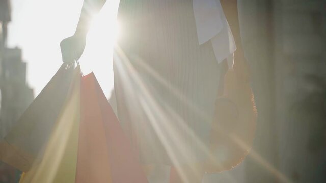 Girl with colorful paper bags after shopping at sunset. Slow motion with sun flares.
