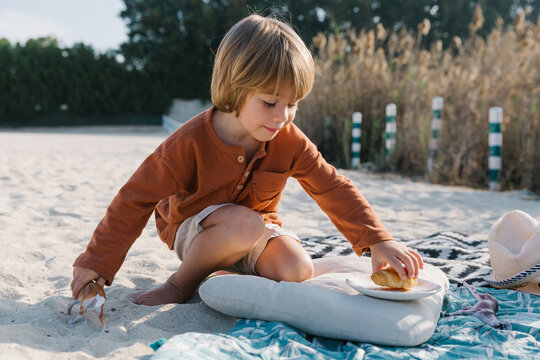 A little boy on the beach is going to eat a croissant