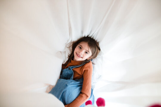 child looking up at the camera surrounded in white curtain