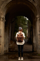 Fototapeta na wymiar rear view on traveler woman with backpack stand in historical ancient arch, exploring interesting old sites and attractions, historical places, at autumn or spring season. view from back.