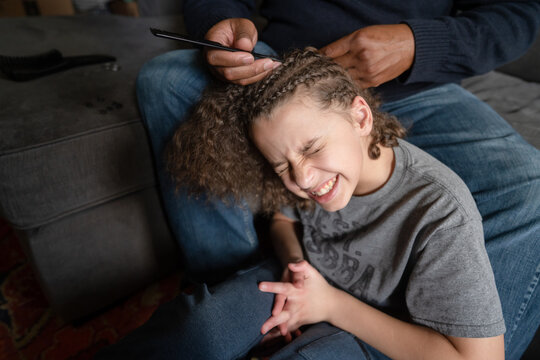 Boy winces in pain as father picks out cornrows