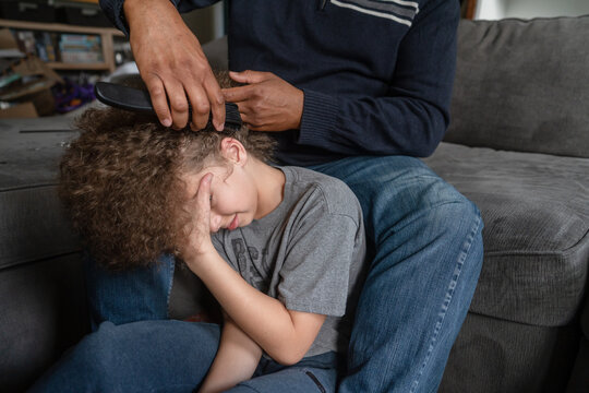 Father brushes out boy's long curly hair